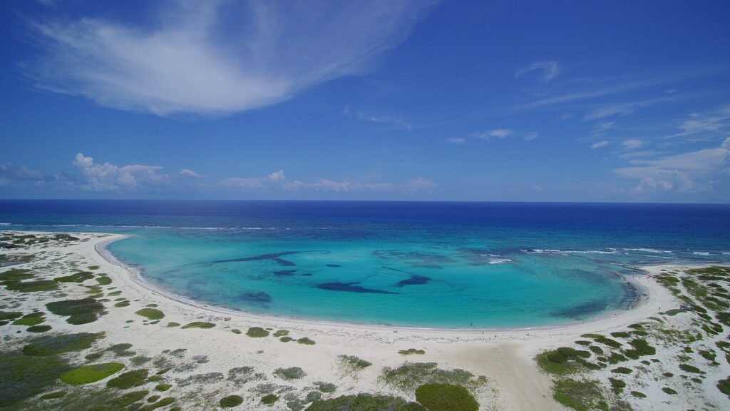 Praia de areias brancas com um plato de águas verdes que vão ficando azuis na região de São Nicolau em Aruba para representar o seguro viagem Aruba