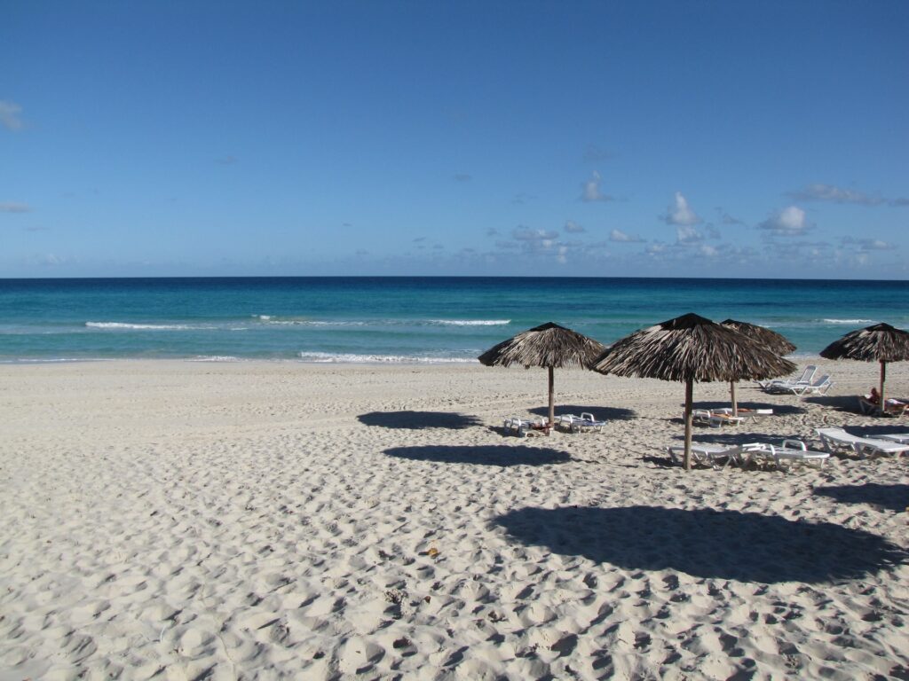 Praia de areia branca e mar azul muito calmo, com guarda-sol feito de bambu presos na areia em Varadero em Cuba para representar seguro viagem para Cuba