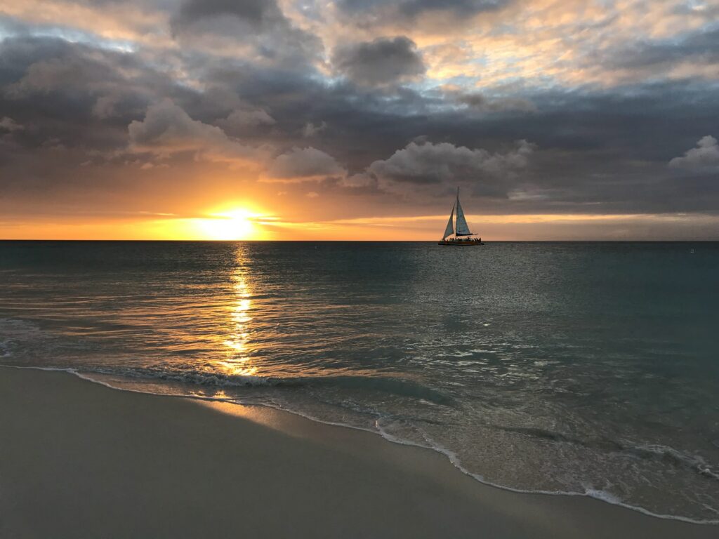 Pôr do sol com vista para o mar e um barco a vela se locomovendo em Eagle Beach em Aruba para representar o seguro viagem para Aruba