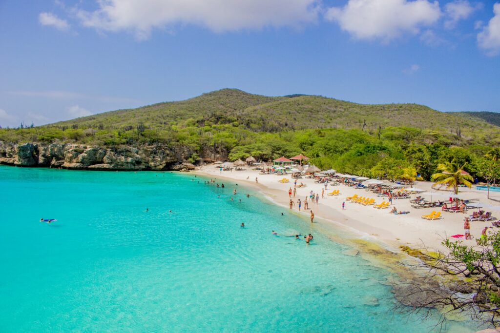 Praia de areia branca e água transparente com turistas se divertindo para representar seguro viagem para o Caribe