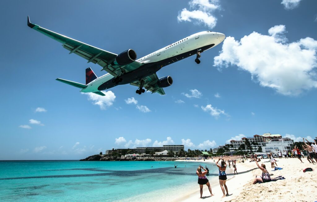 Avião passando muito baixo numa praia com águas transparentes e areia branca enquanto os turistas tiram fotos na Ilha de São Martinho no Caribe