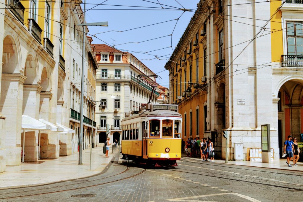Um bondinho amarelo pelas ruas centrais de Lisboa, pessoas caminhando, para representar o seguro viagem para Portugal