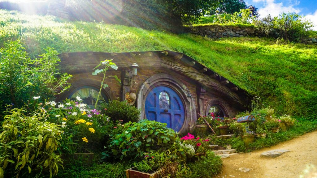Cenário da casa de um hobbit do filme "Senhor dos Anéis" em Matamata na cidade de Waikato, com uma porta azul redonda, um jardim na frente, cercada de vegetação, para representar um seguro viagem para Nova Zelândia