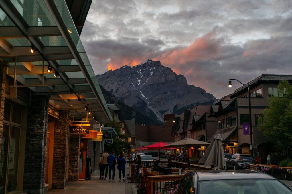 Área central de Banff com montanhas aso fundo numa rua movimentada, com lojas e restaurantes para representar seguro viagem para Banff no Canadá