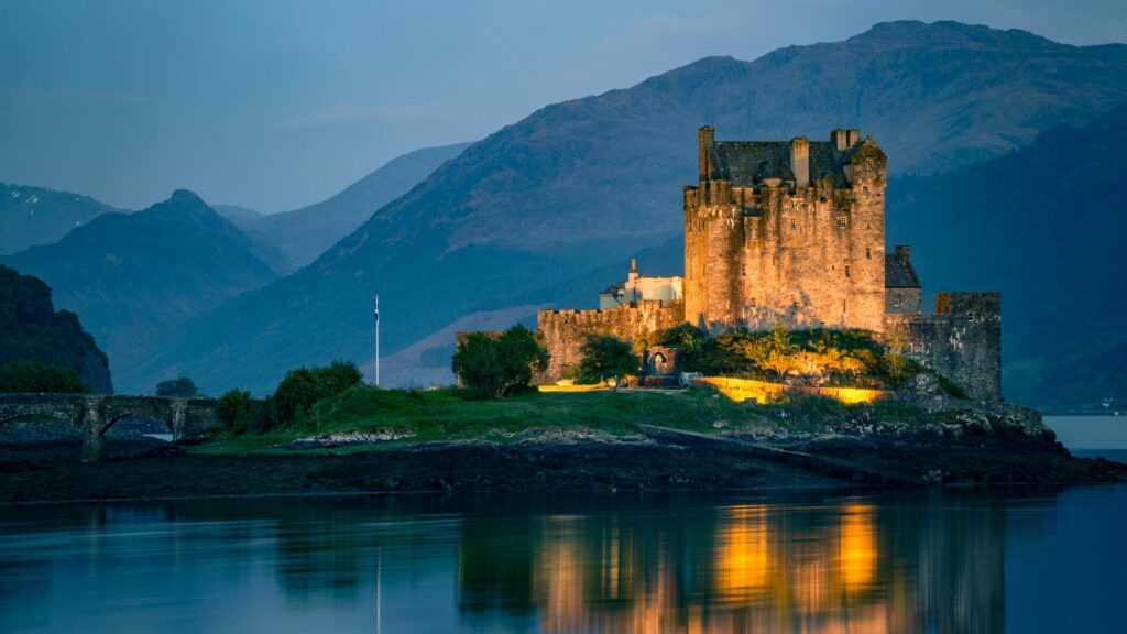 Um castelo iluminado de noite em Dornie, com montanhas atrás e cercado por águas, na Escócia