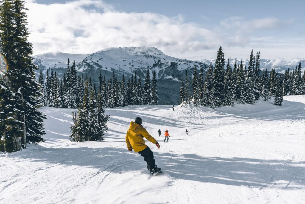 Montanhas nevadas e pinheiros cobertos também de neve, pessoas praticando snowboard em uma estação de esqui em Whistler no Canadá 