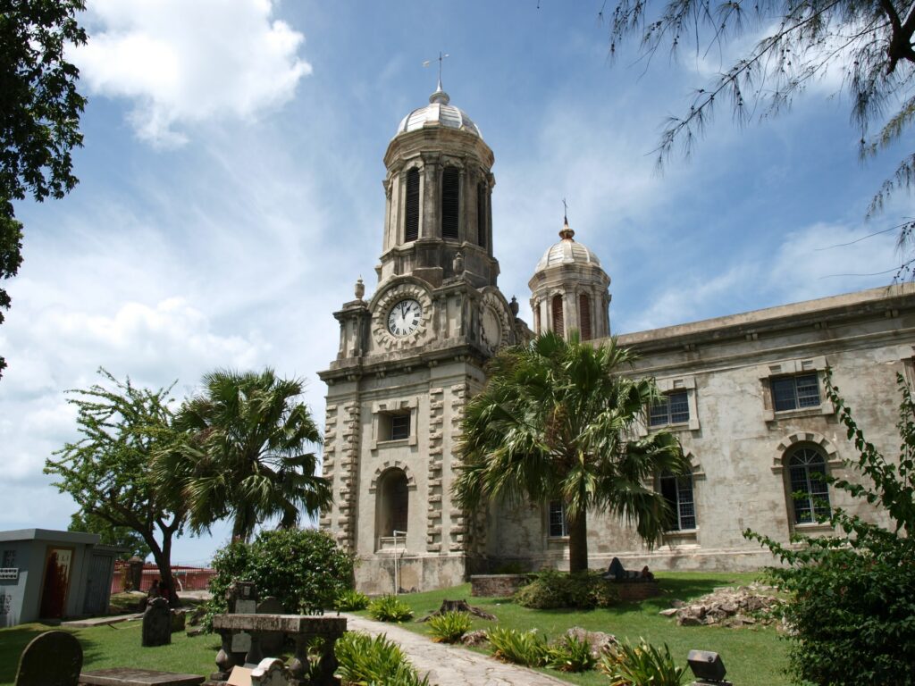 Igreja de arquitetura antiga na ilha de Antígua e Barbuda cercada por coqueiros e um relógio em sua torre central para representar o seguro viagem para Antígua e Barbuda