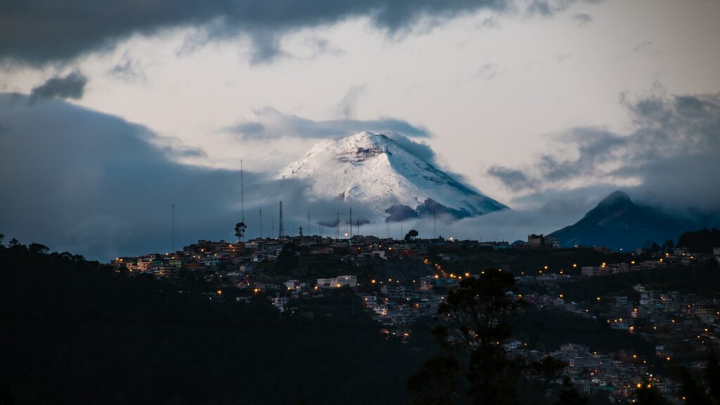 Cidade no fim do dia com uma enorme montanha nevada do vulcão Cotopaxi ao fundo para representar seguro viagem em Quito