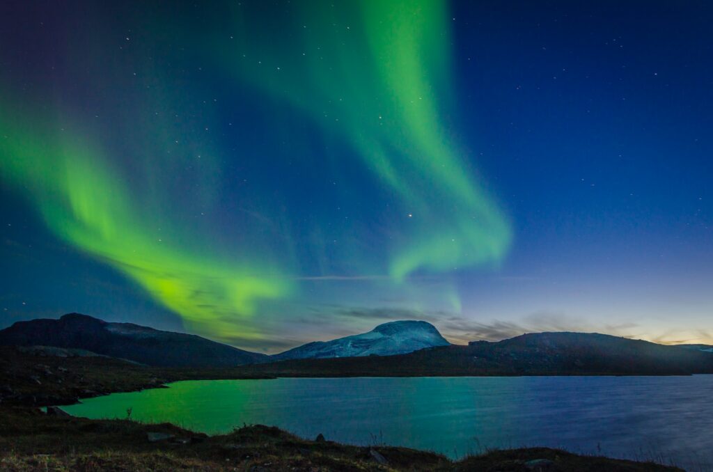 Aurora boreal no Abisko National Park na Suécia com montanhas e um céu em verde, roxo e azul para representar o melhor seguro viagem para Europa