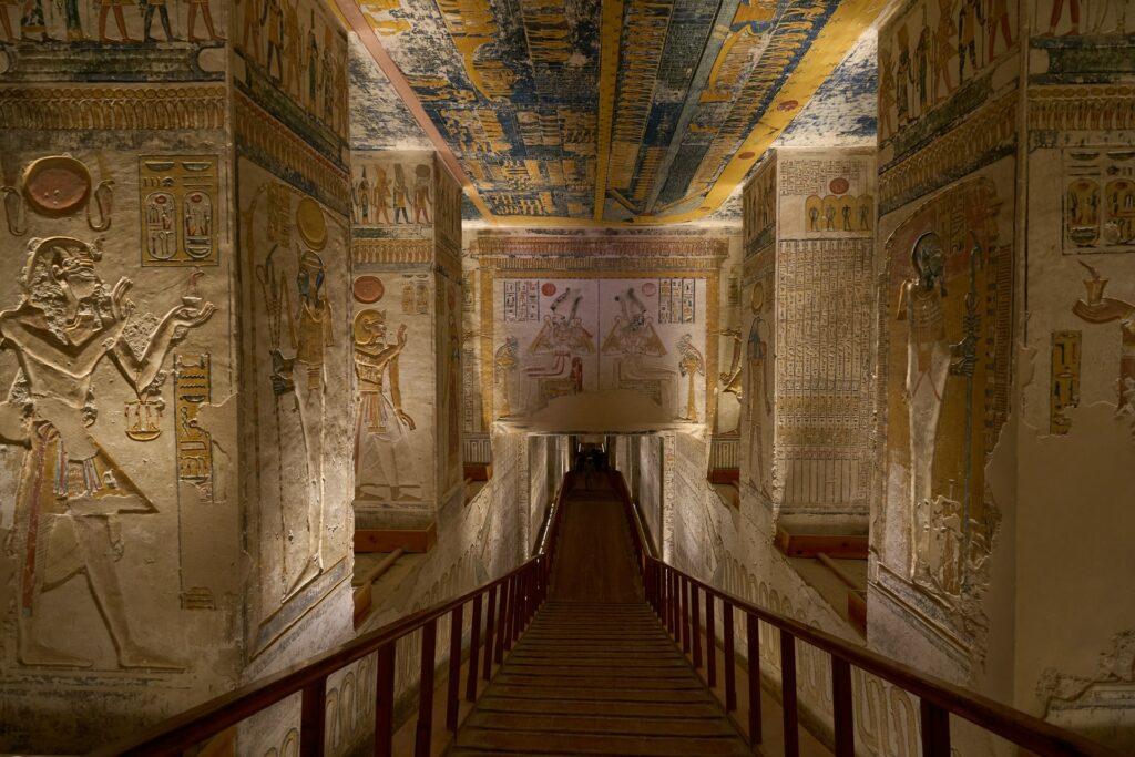 Parte interna do Vale dos Reis do Egito na cidade de Luxor com pinturas nas paredes de faraós, uma escadaria passa no meio, formando um corredor e nas laterais estão as obras pintadas ou esculpidas nas paredes, para representar o seguro viagem para o Egito