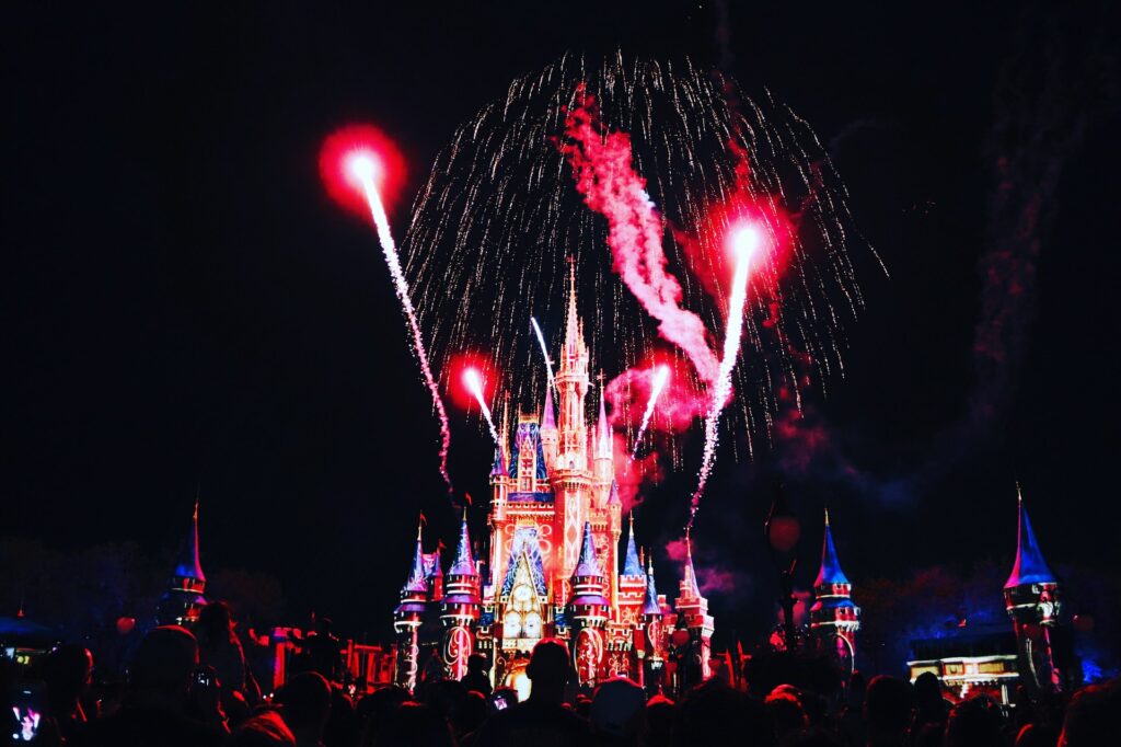 O castelo Magic Kingdom símbolo dos parques de diversão da Disney em Orlando, de noite com todas suas luzes acessas e fogos de artificio vermelhos brilhando no céu para representar o seguro viagem para Flórida