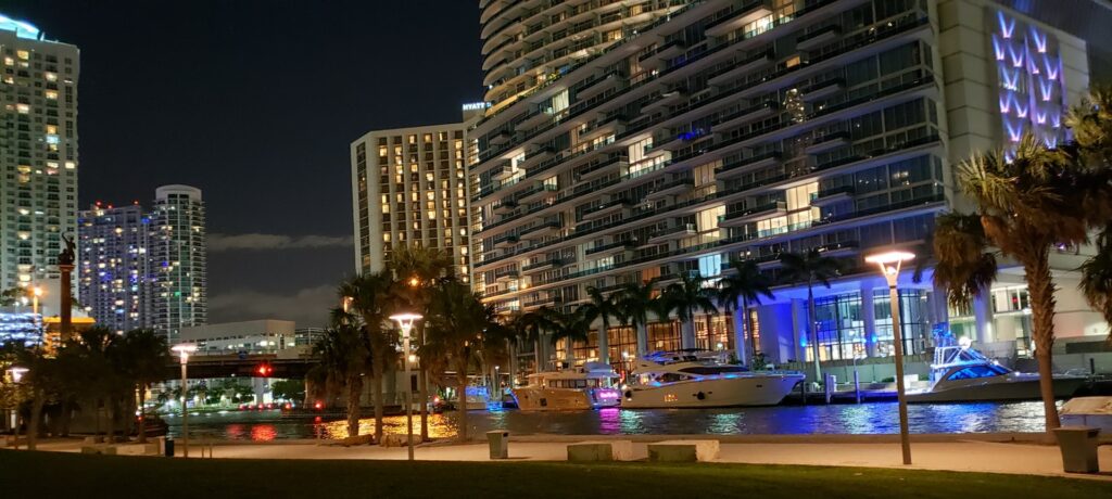 Prédios luxuosos na beira de um pequeno canal com lanches estacionadas, outros prédios iluminados ao redor, na região de Downtown Miami para representar o seguro viagem para Miami