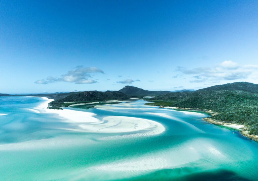 Uma praia com mar em tons de azul claro e branco em Whitsunday Islands em Queensland, cercada por natureza