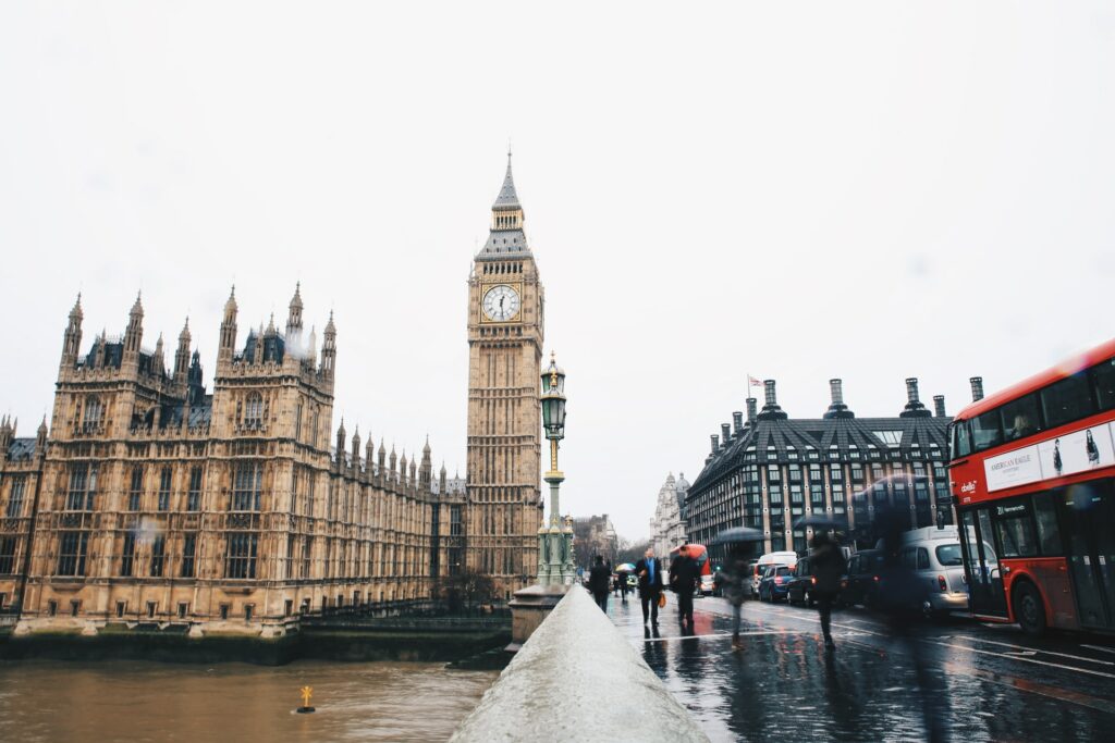 Construção icônica com a torre do relógio do Big Ben em Londres, pessoas andando na calçada, ônibus, um dia nublado, para representar o seguro viagem para Londres