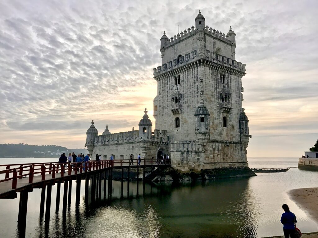 Torre de Belém, construção antiga em estilo romano, no mar, com uma ponte que leva as pessoas em direção do monumento, em Lisboa em Portugal