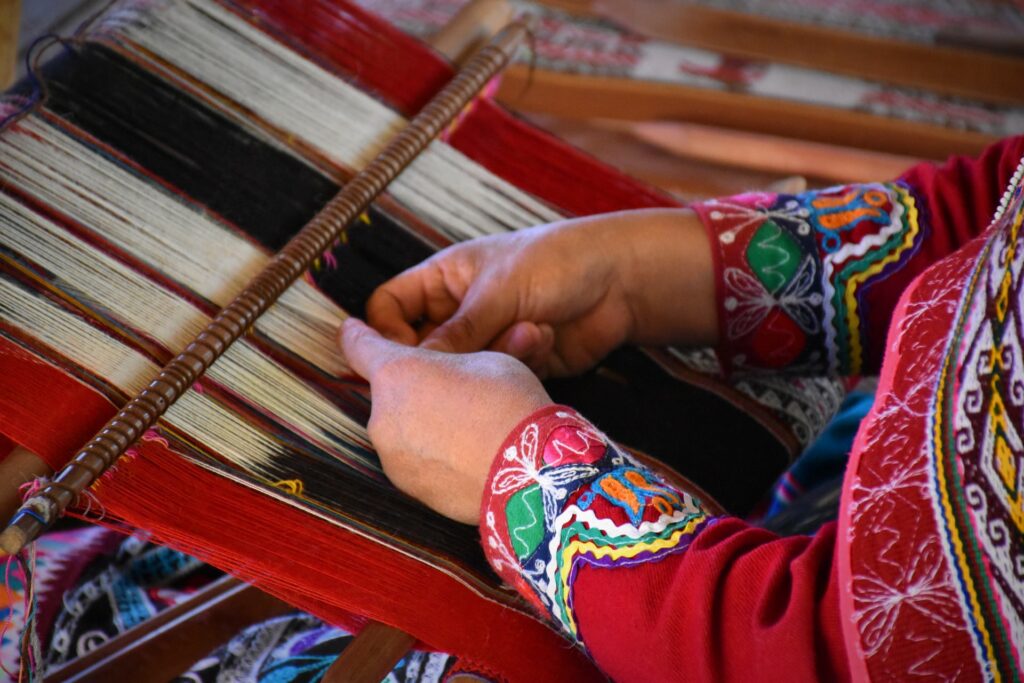 Mãos de uma artesã peruana mexendo em um tear com fios de algodão peruano para fazer alguma peça de roupa para representar o seguro viagem para Cusco