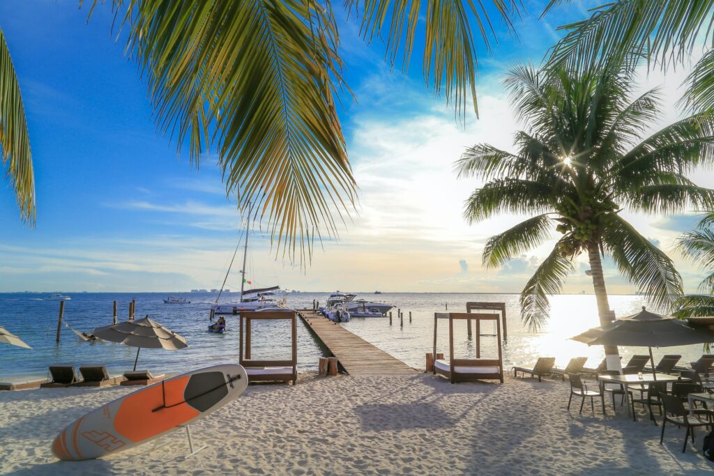 Um deck que sai da praia para o mar, muitas cadeiras, pranchas de surf e mesas na areia em Quintana Roo para representar seguro viagem para Isla Mujeres