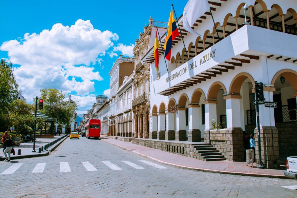 Uma rua com prédios históricos, carros, ônibus e pessoas passando em Cuenca, uma cidade no sul do Equador