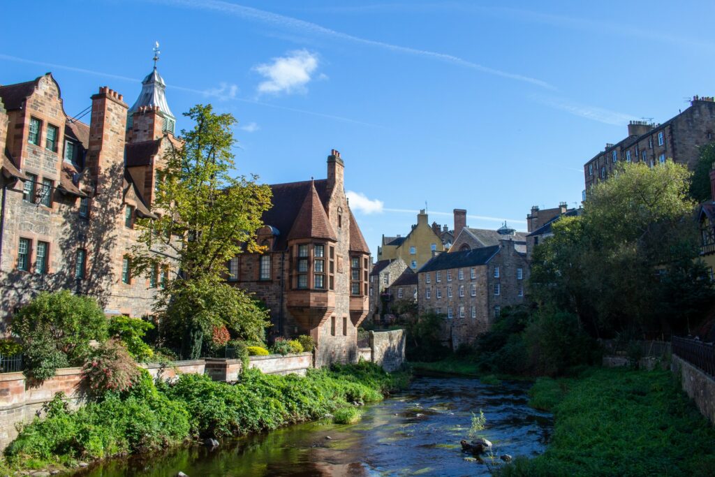 Um lago passando por entre a cidade de Edimburgo, capital da Escócia, com casas em construção antiga de tijolos vermelhos, muita vegetação, para representar o seguro viagem para Escócia