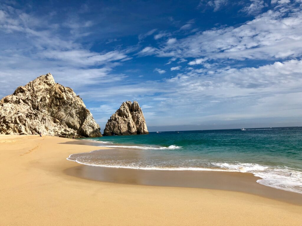 Praia com mar azul escuro, areia bege e com formações rochosas se misturando entre terra e mar na Playa del Divorcio em Los Cabos no México para representar o seguro viagem para Los Cabos