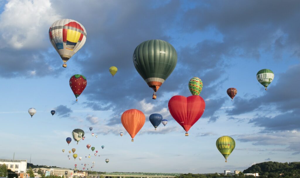 Diversos balões coloridos no ar, sob uma cidade na Lituânia, os balões são coloridos e em formatos variados, para representar o seguro viagem para Lituânia