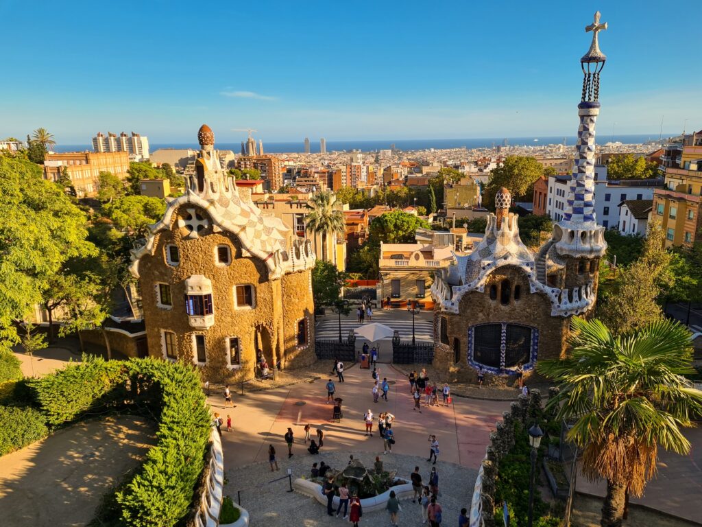 Parque Güell em Barcelona com construções antigas e cheias de ondulações nas portas e janelas do arquiteto Antoni Gaudí, muitas árvores e pessoas caminhando