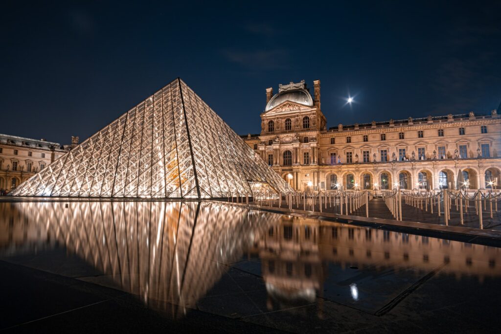 Museu do Louvre na França de noite com suas luzes acesas e seu reflexo no lago artificial, para representar o seguro viagem para Europa