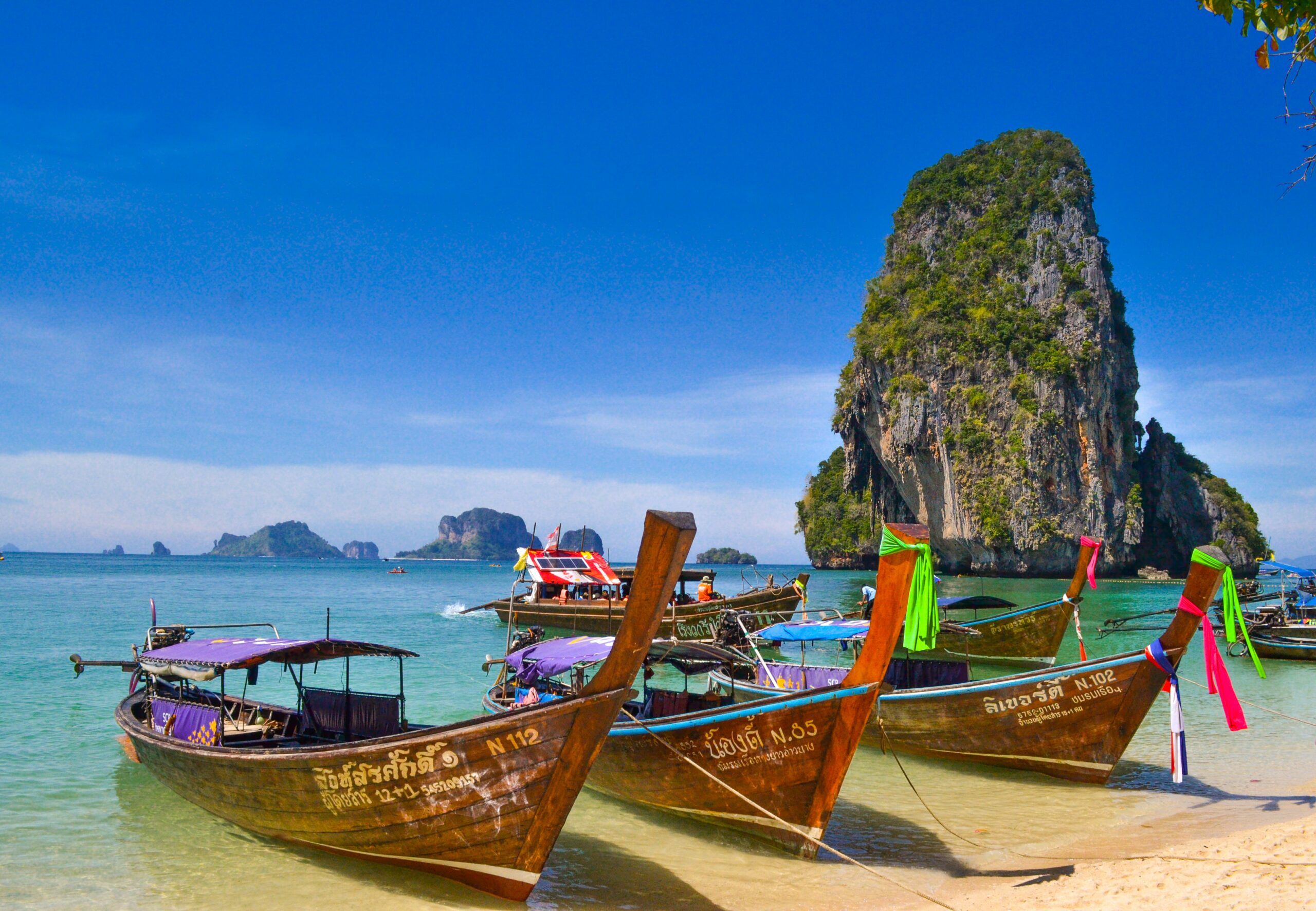Praia azul turquesa com barcos parados na areia em Phra Nang Beach, Krabi, Tailândia.