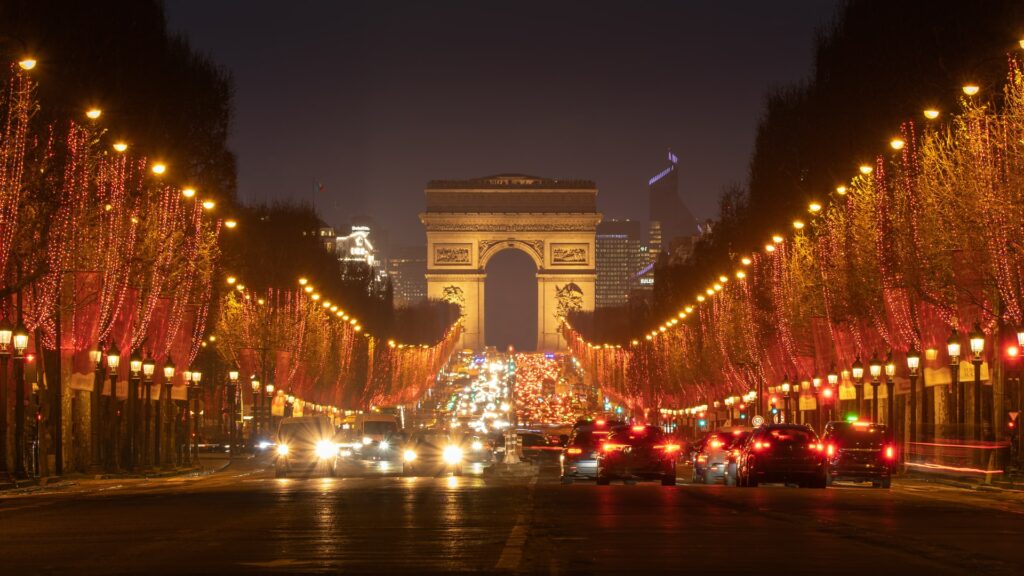 Avenue des Champs Élysées na França, uma enorme avenida cercada de pinheiros com luzes de natal que levam em direção a um monumento histórica em formato de arco para representar o seguro viagem para França