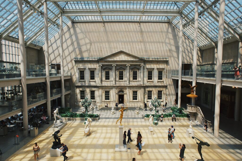 Metropolitan Museum of Art com um teto inteiro de vidro e uma arquitetura colonial com pilastras e diversos monumentos espalhados numa espécie de pátio em Nova York