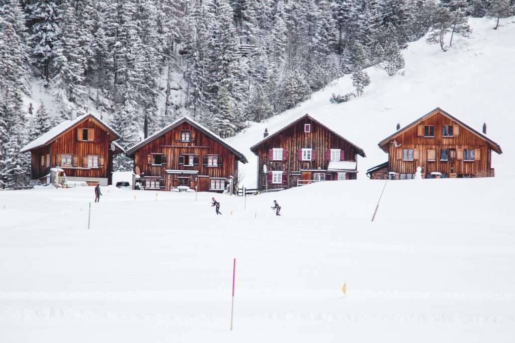 Uma pequena estação de esqui na Vila Steg com quatro casas de madeira cobertas e cercadas por neve e algumas pessoas esquiando, para representar o seguro viagem para Liechtenstein
