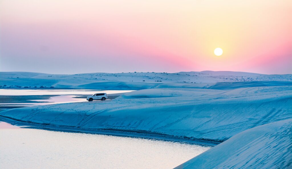 Deserto de Doha com pequenas dunas, águas e o sol de pondo ao fundo, para representar o seguro viagem para Qatar