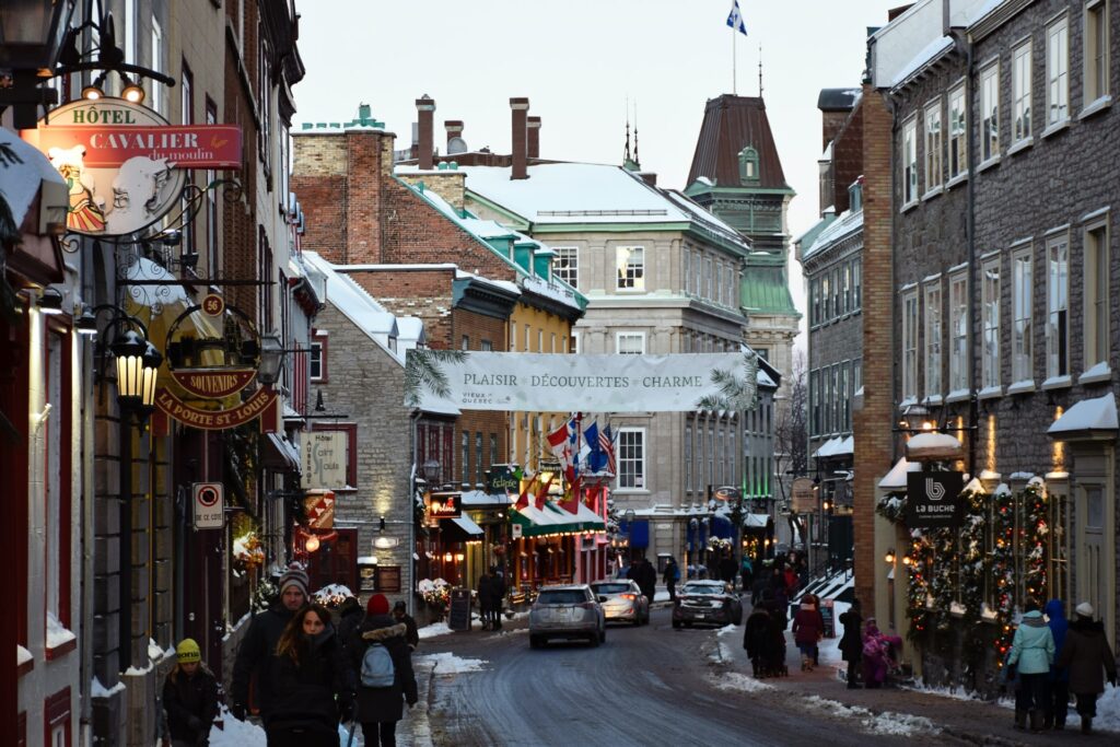Ruas centrais de Quebec com estilo vitoriano, bandeiras, torres históricas, restaurantes e pessoas caminhando para representar o seguro viagem para Quebec