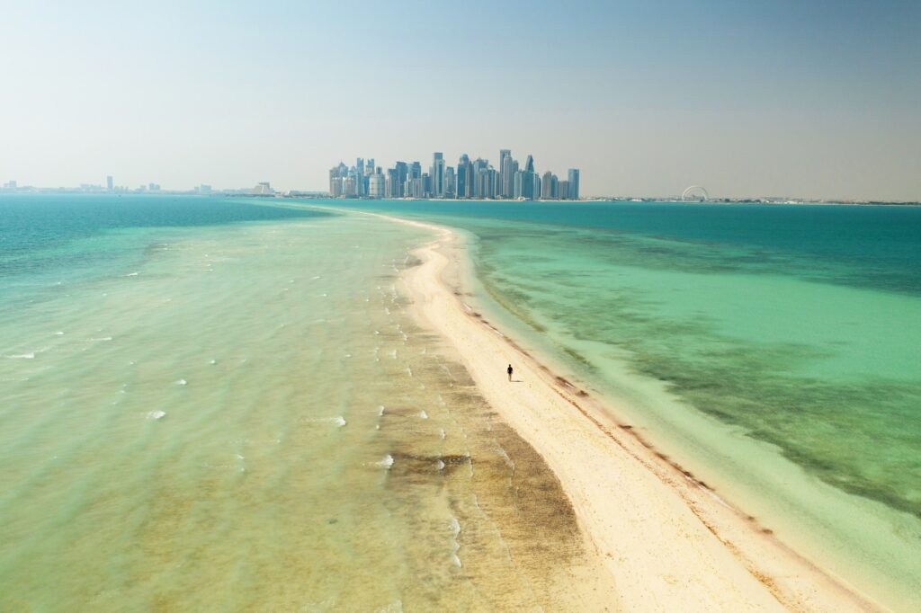 Ilha de Al Safliya na costa de Doha na capital do Qatar, uma linha de areia cercada por águas cristalinas que levem em direção de uma cidade, para representar o seguro viagem para Qatar