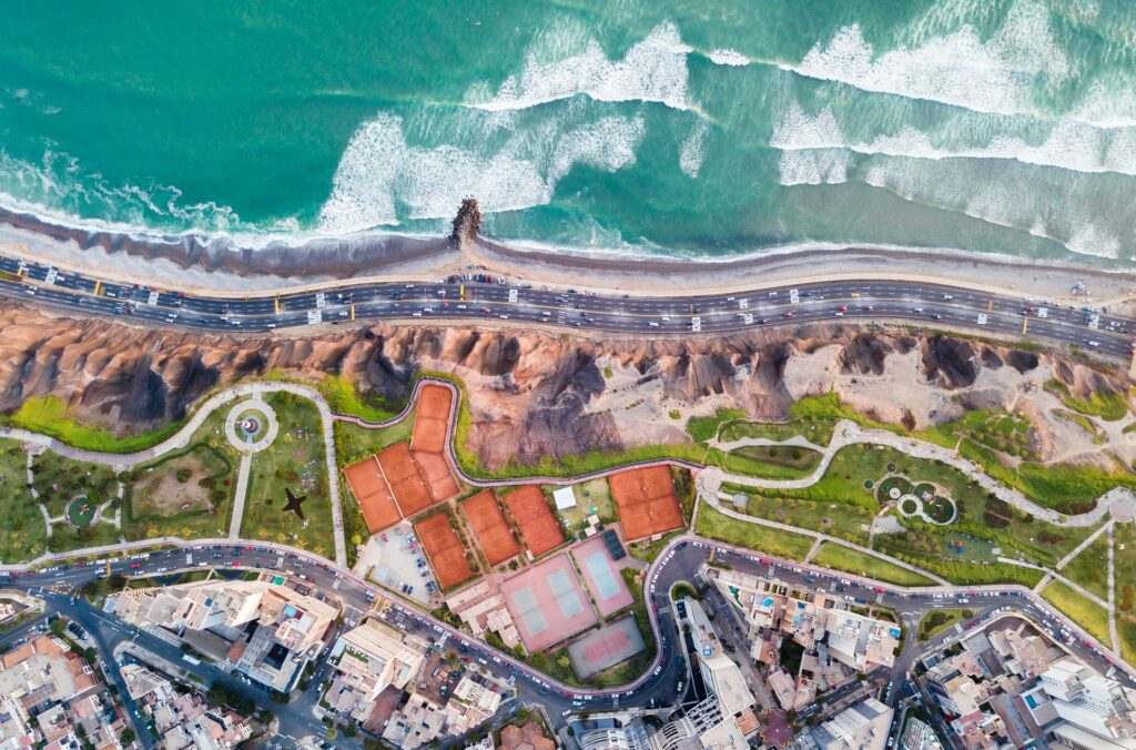 Imagem do alto de Malecon Cisneros, em Miraflores, região de Lima no Peru, com o mar, uma estrada e a cidade logo em seguida