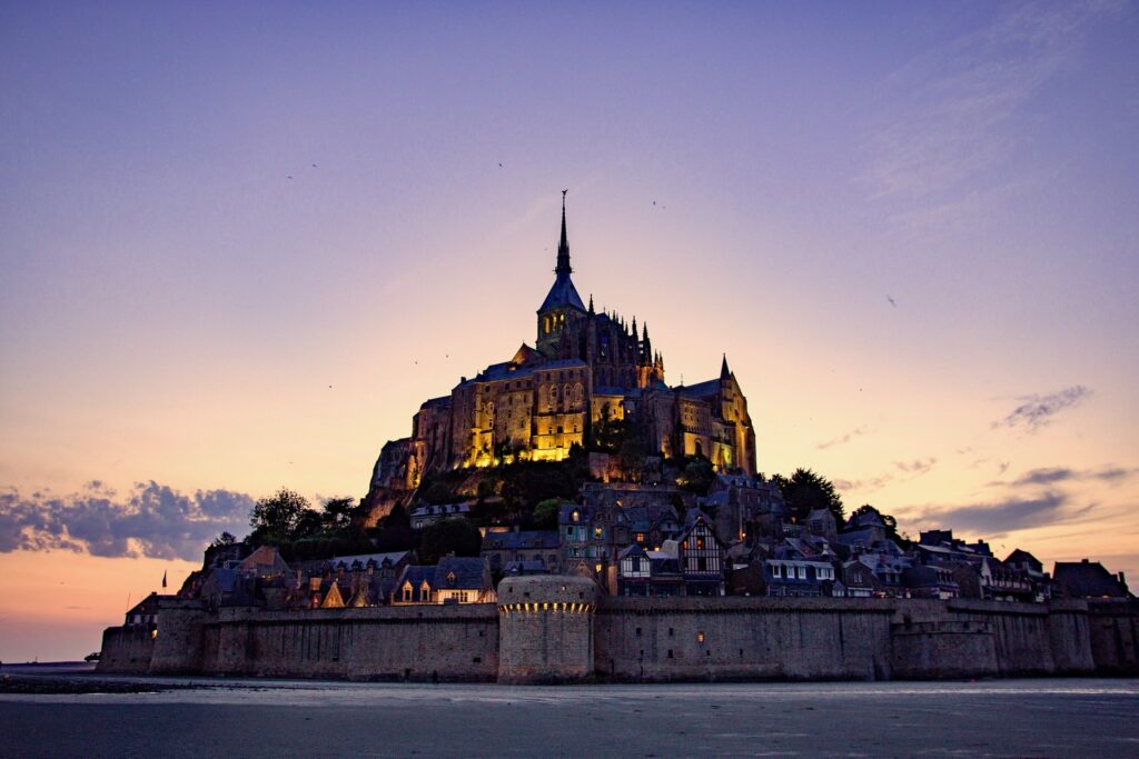 Mont Saint Michel na França uma construção antiga em estilo colonial com as luzes acesas de noite para representar o seguro viagem para França