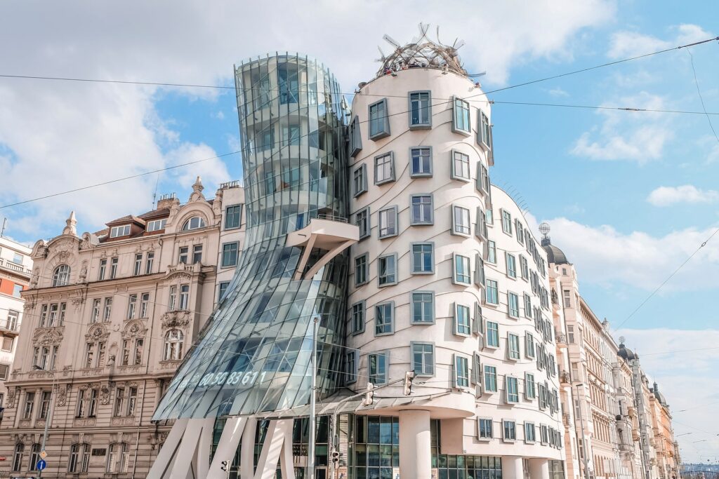 Casa Dançante, uma construção arquitetônica curiosa em que duas torres em formato arredondado estão lado a lado, com janelas em desníveis e não em linha reta, e uma das torres em a parte baixa torta, causando uma impressão que ela está caindo, para representar o seguro viagem para Praga
