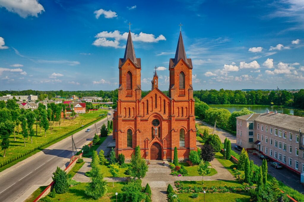Igreja em Minory, uma cidade de Belarus, em tons de laranja e marrom, com um jardim ao redor, numa região verde, com lagos e construções mais antigas, para representar o seguro viagem para Belarus
