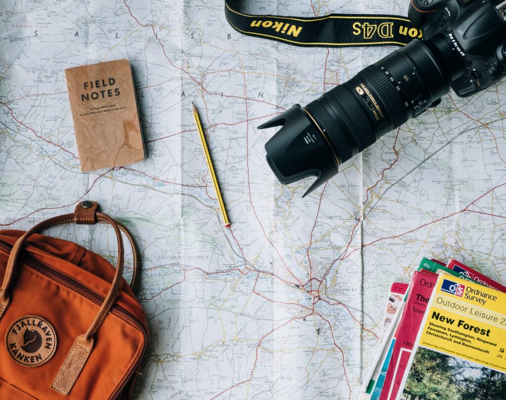 Uma mesa com um mapa aberto, um lápis, um caderno, uma mochila e uma câmera fotográfica em cima do mapa, para representar o seguro viagem para Brunei