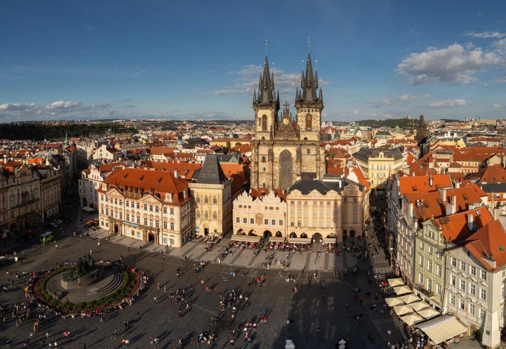 Praça da Cidade Velha em Praga, local com um enorme pátio, uma fonte, cercado por prédios antigos e uma enorme catedral, muitas pessoas caminhando, para representar o seguro viagem para Praga