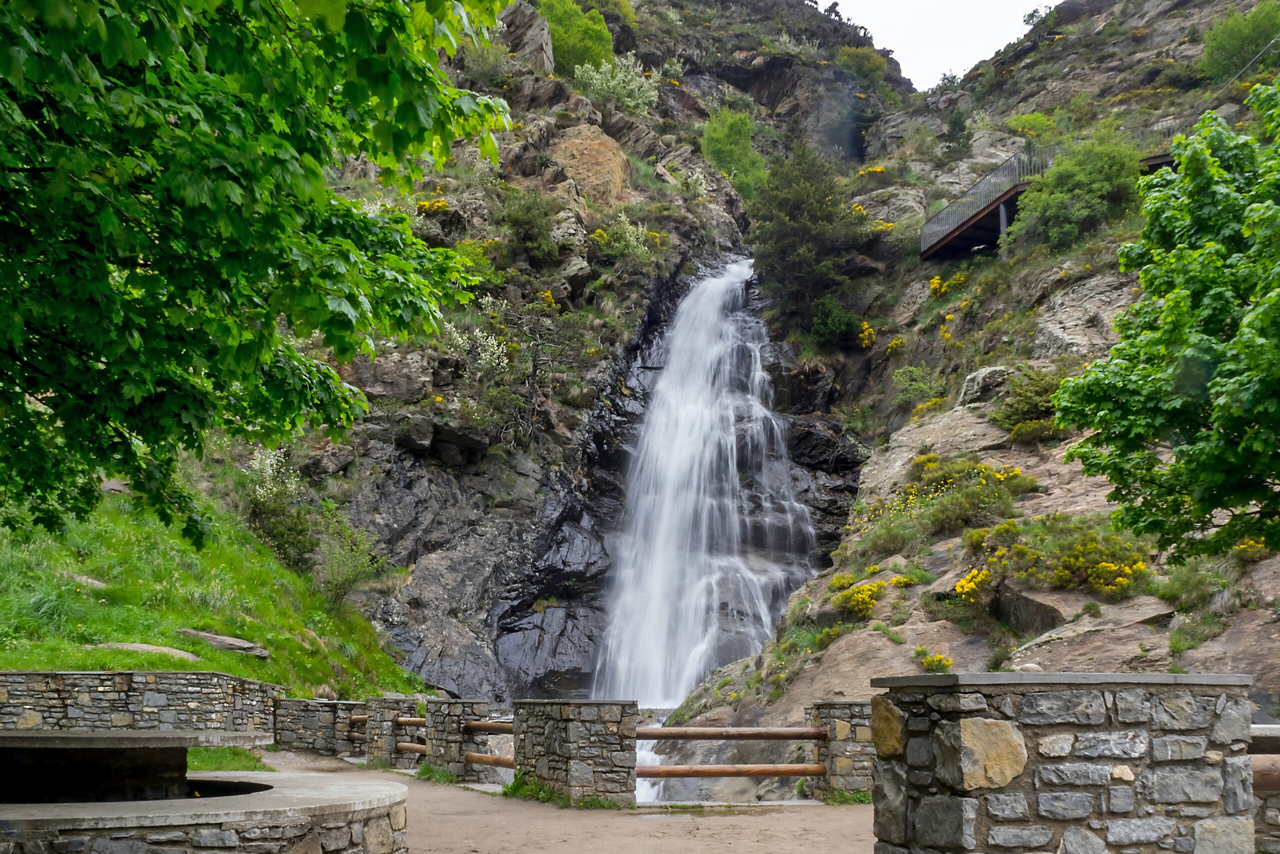 Cachoeira des Moles cercada de vegetação e uma mureta de pedra para observação em Andorra