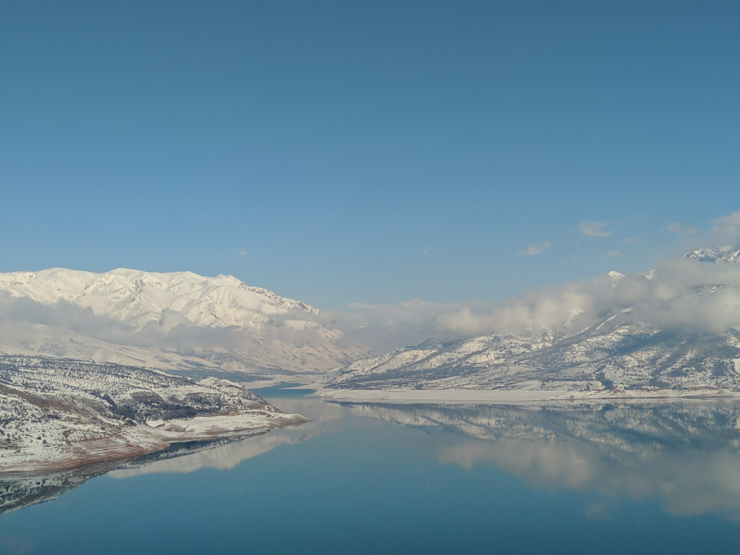 Montanhas com neve atrás de um grande lago calmo refletindo o céu azul em Uzbequistão - Representa seguro viagem Uzbequistão.