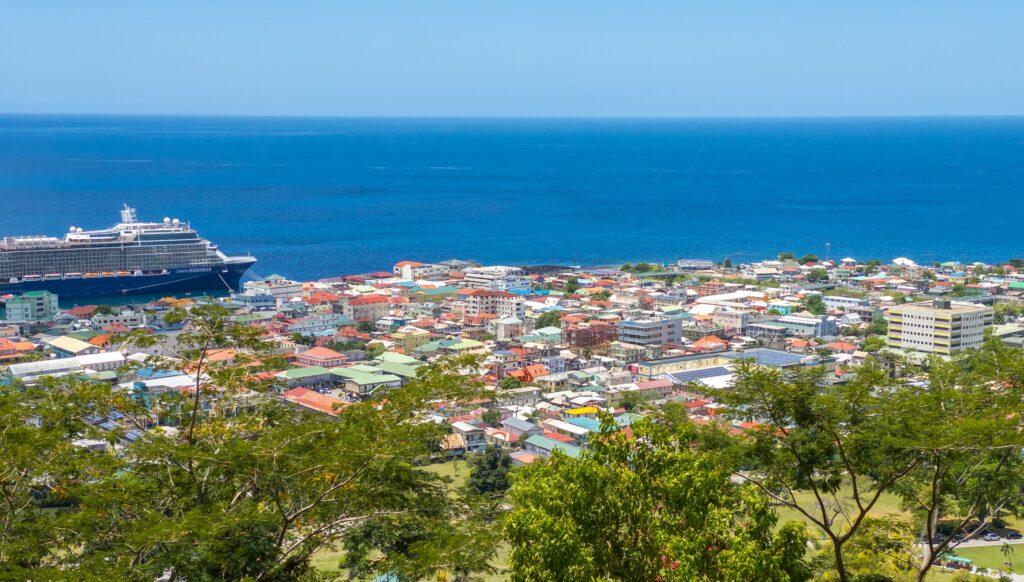 Vista da cidade de Roseau, Dominica com casas e prédios e um navio parado na costa do mar. Representa seguro viagem para Dominica.

