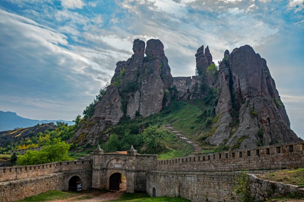 O Castelo Belogradchik próximo de uma enorme montanha com uma elevação rochosa cercada por natureza, para representar o seguro viagem para Bulgária