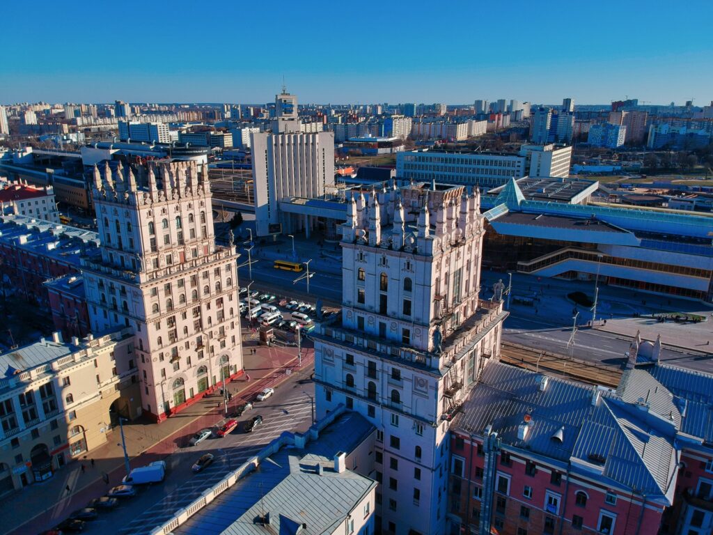 Minsk, capital de Belarus, dois prédios históricos se destacam pela arquitetura, nas ruas passam carros e ônibus, alguns prédios comerciais ao redor, para representar o seguro viagem para Belarus