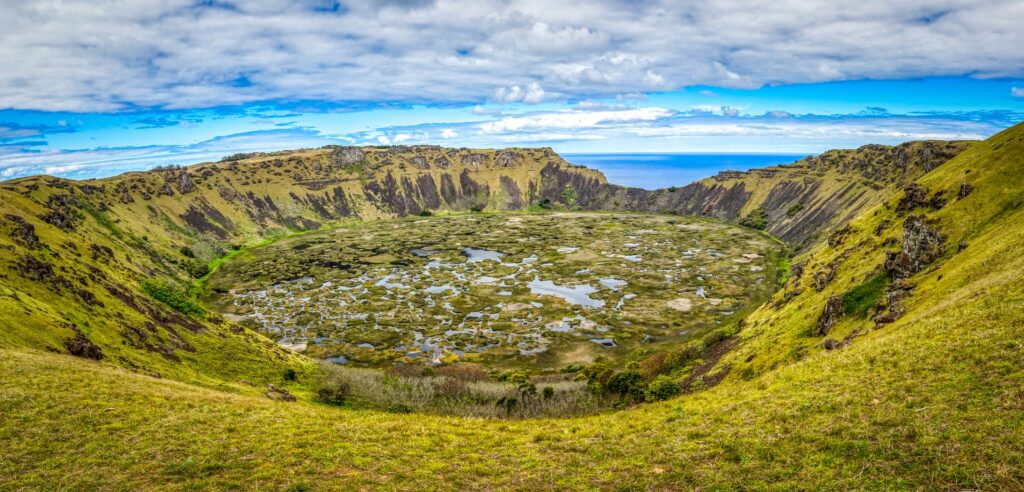 O extinto vulcão Rano Kau, a cratera continua existindo e é enorme, no centro dela é possível ver água que se acumulou e deu origem a vegetação, ao redor, as montanhas também são cobertas por uma espessa camada de vegetação que quase se parece com lodo, para representar o seguro viagem para Ilha de Páscoa