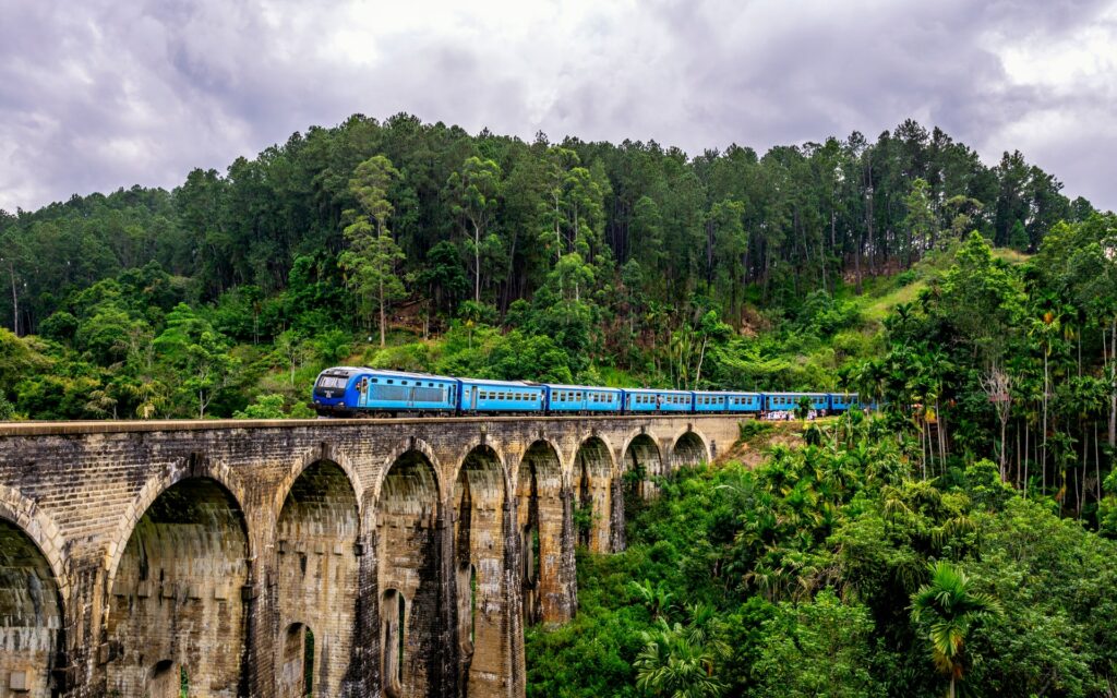 Um trem azul atravessando uma ponte envelhecida e cercada por muita vegetação, para representar o seguro viagem para o Sri Lanka