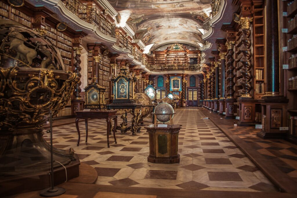 Parte interna da Biblioteca Nacional, arquitetura antiga e renascentistas, globos terrestres de vidro, muitos livros em prateleiras cor de ouro, um teto com pinturas à mão e no formato arredondado, para representar o seguro viagem para Praga