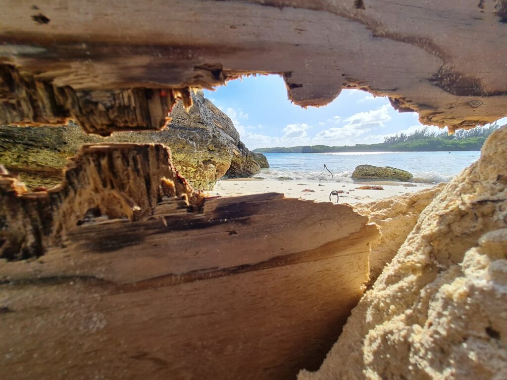 Uma foto tirada de dentro de uma gruta com rochas claras que está em direção de uma praia de águas claras