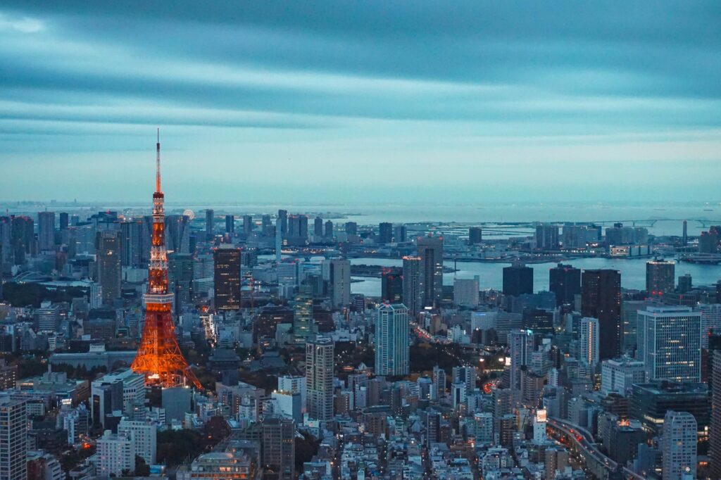 Torre de Tóquio acesa no fim da tarde, se destacando entre os prédios iluminados, para representar o seguro viagem para Tóquio